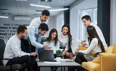 Guy shows document to a girl. Group of young freelancers in the office have conversation and working.